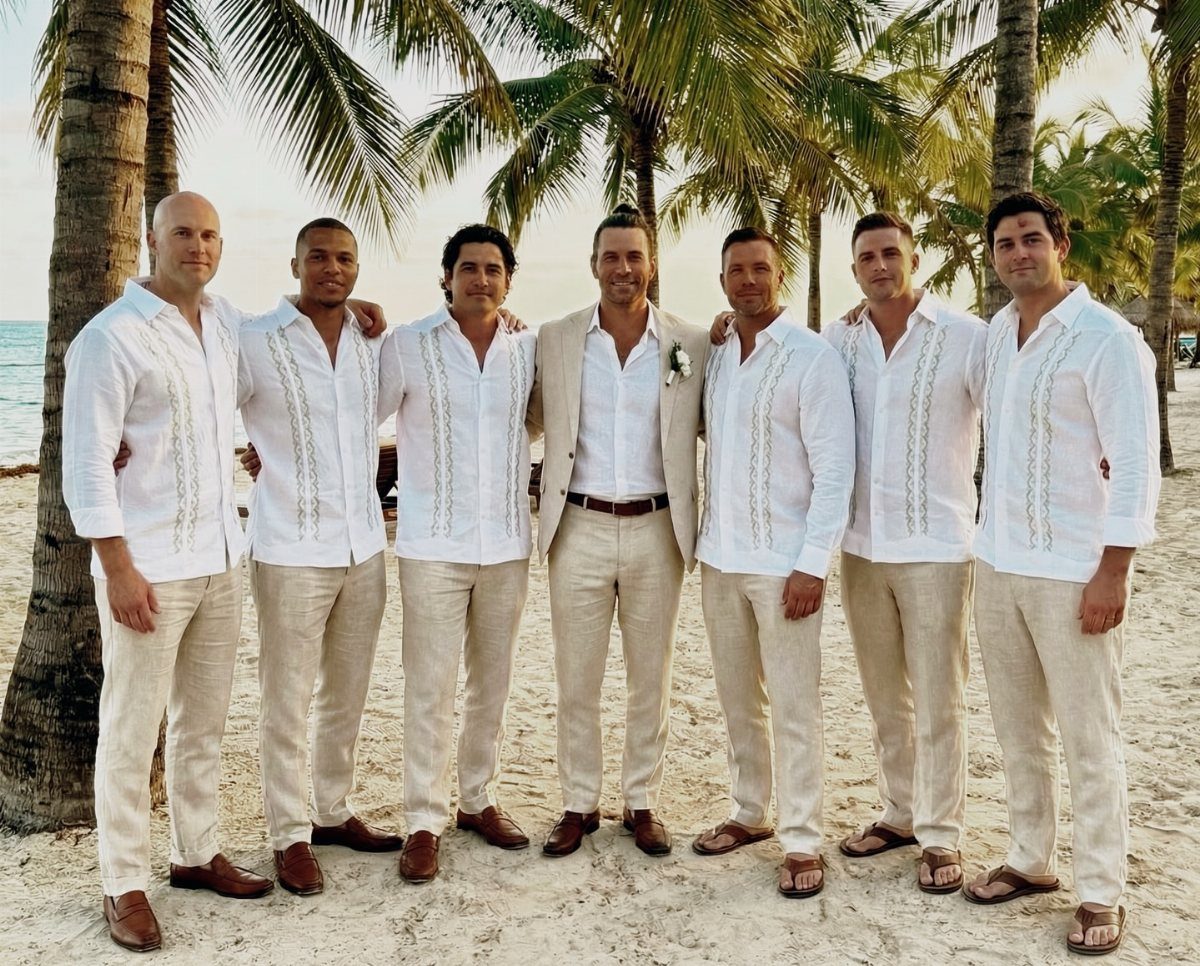 Groom and groomsmen wearing white shirts and beige linen pants on a beach.