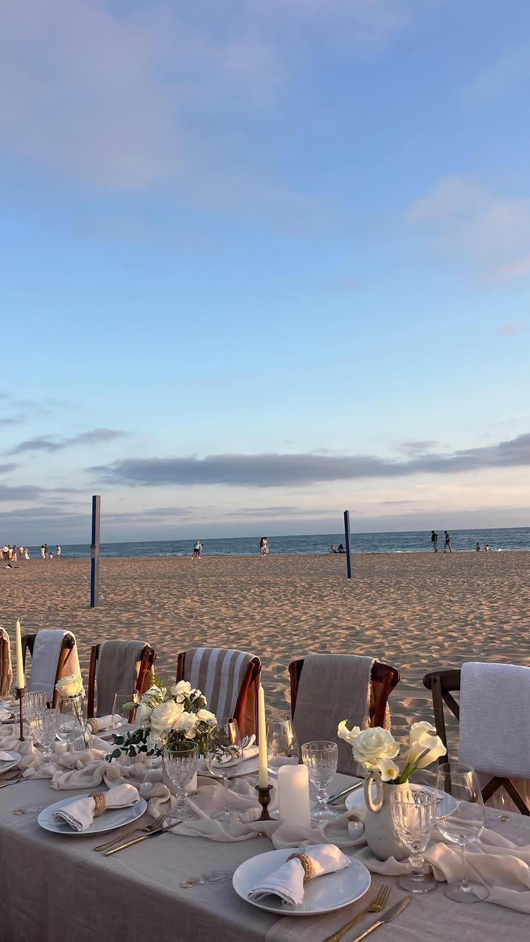 Formal dining table with white flowers and candles set up on a sandy beach