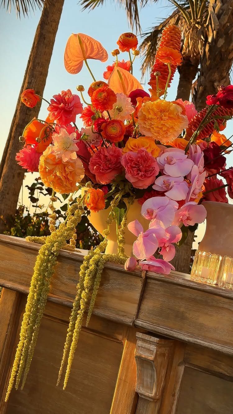 Vibrant orange, pink, and yellow floral arrangement on a rustic wooden table outdoors.