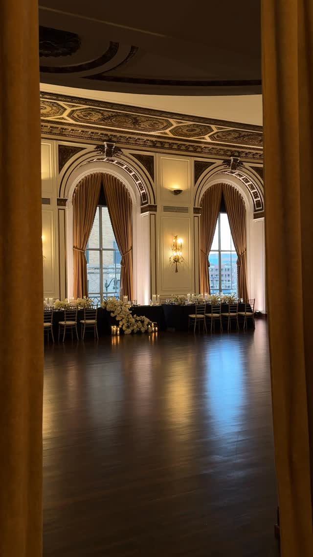 Ornate ballroom with gold molding, arched windows, and formal banquet table settings.