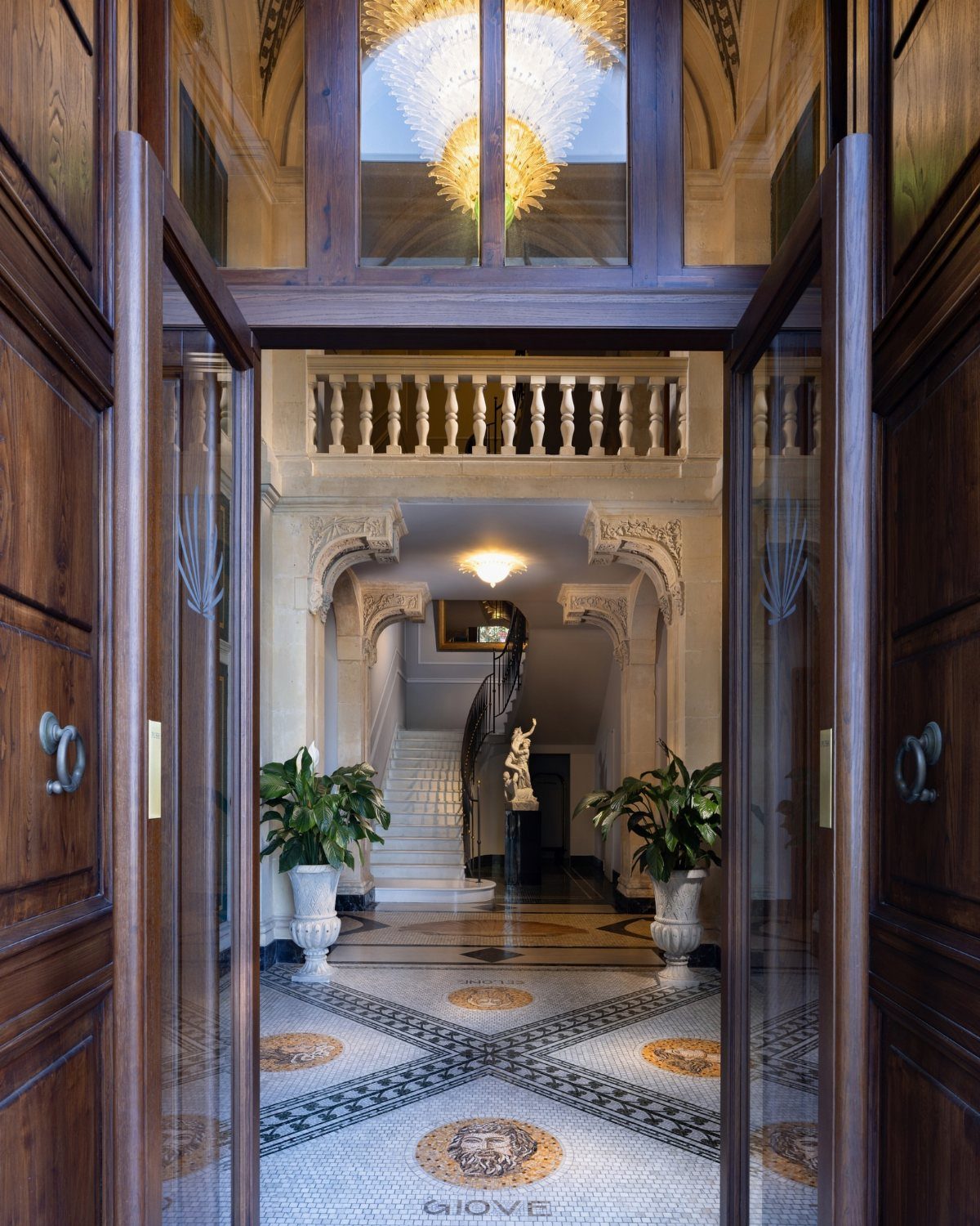 Grand hotel lobby with mosaic tile floors, stone columns, and dark wood doors.