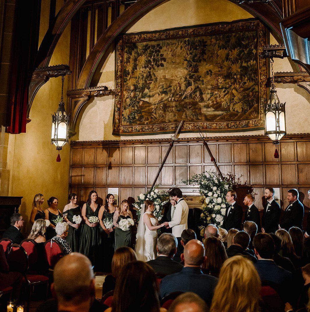 Wedding ceremony in a historic hall with wood paneling and a large tapestry.
