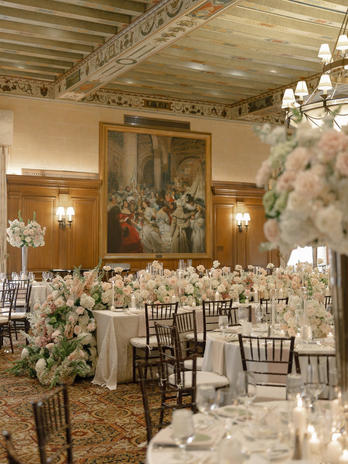 Opulent ballroom with white floral table runners, wood paneling, and a painted ceiling.
