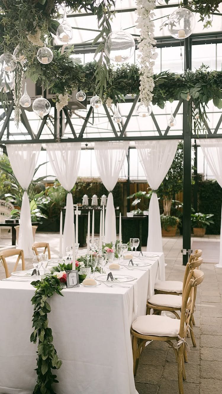 Wedding table setting with white linens and greenery inside a lush botanical conservatory