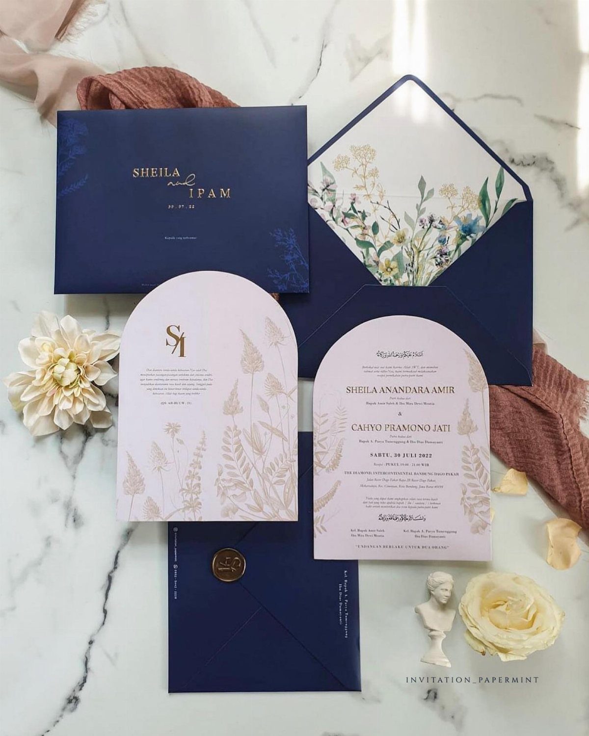 Navy blue and blush pink wedding invitation set with floral designs on marble.
