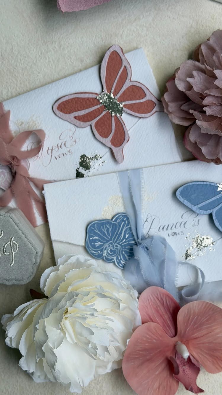 White wedding invitations with pink and blue cutouts surrounded by fresh peonies.