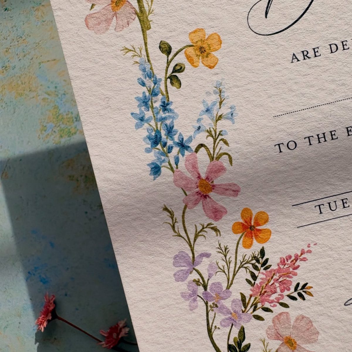 Watercolor wildflower invitation with blue, pink, and yellow floral designs on textured paper.