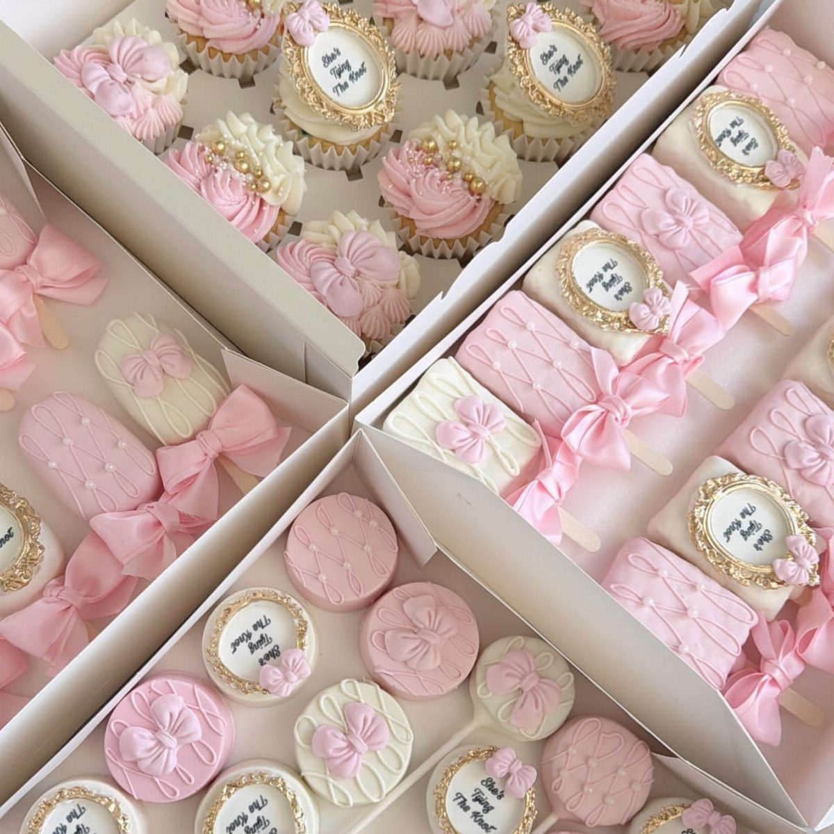 Pink and white cupcakes and cake pops decorated with ribbons in white boxes.
