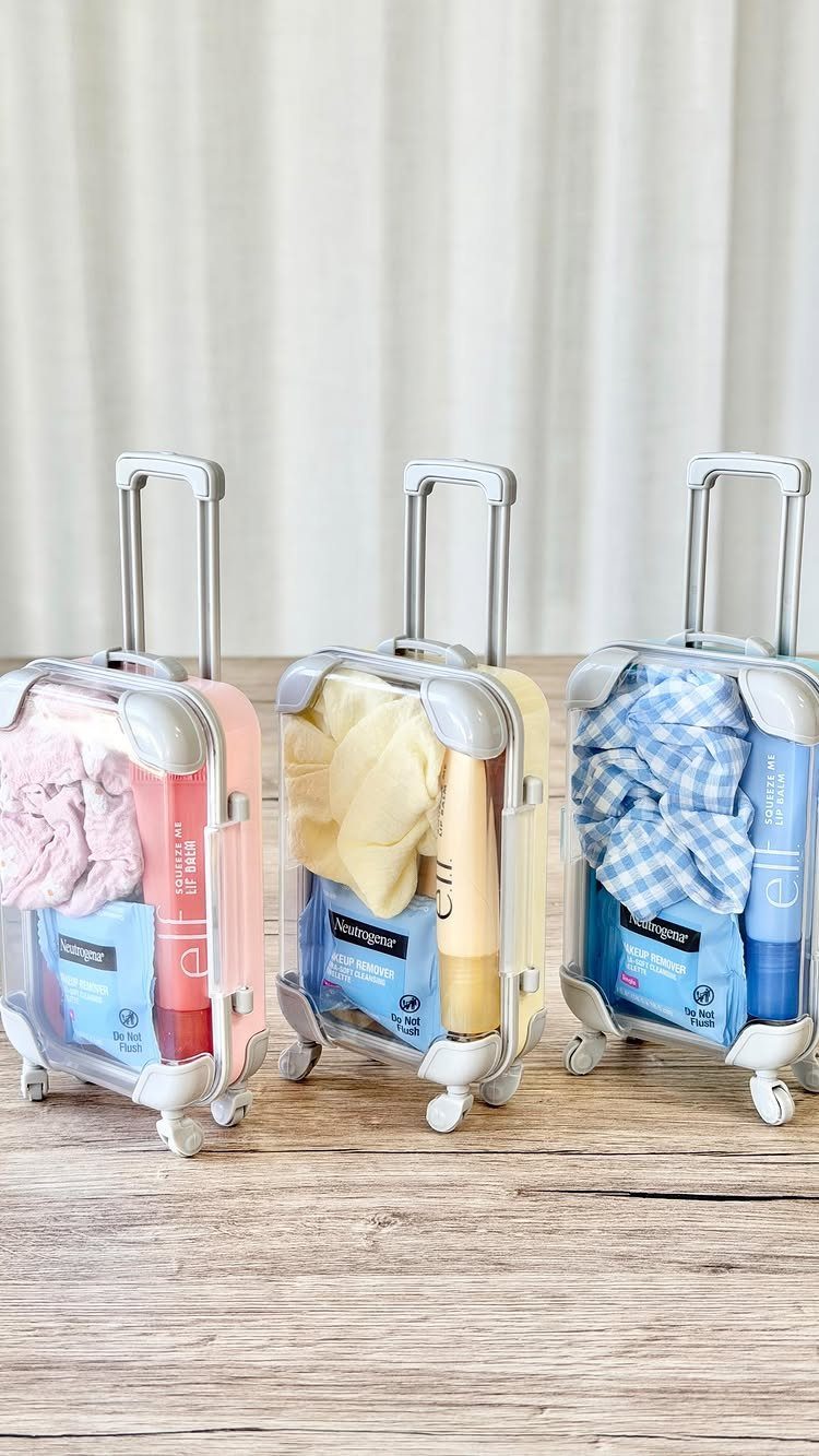 Three miniature suitcases filled with small towels and beauty products on wooden table.