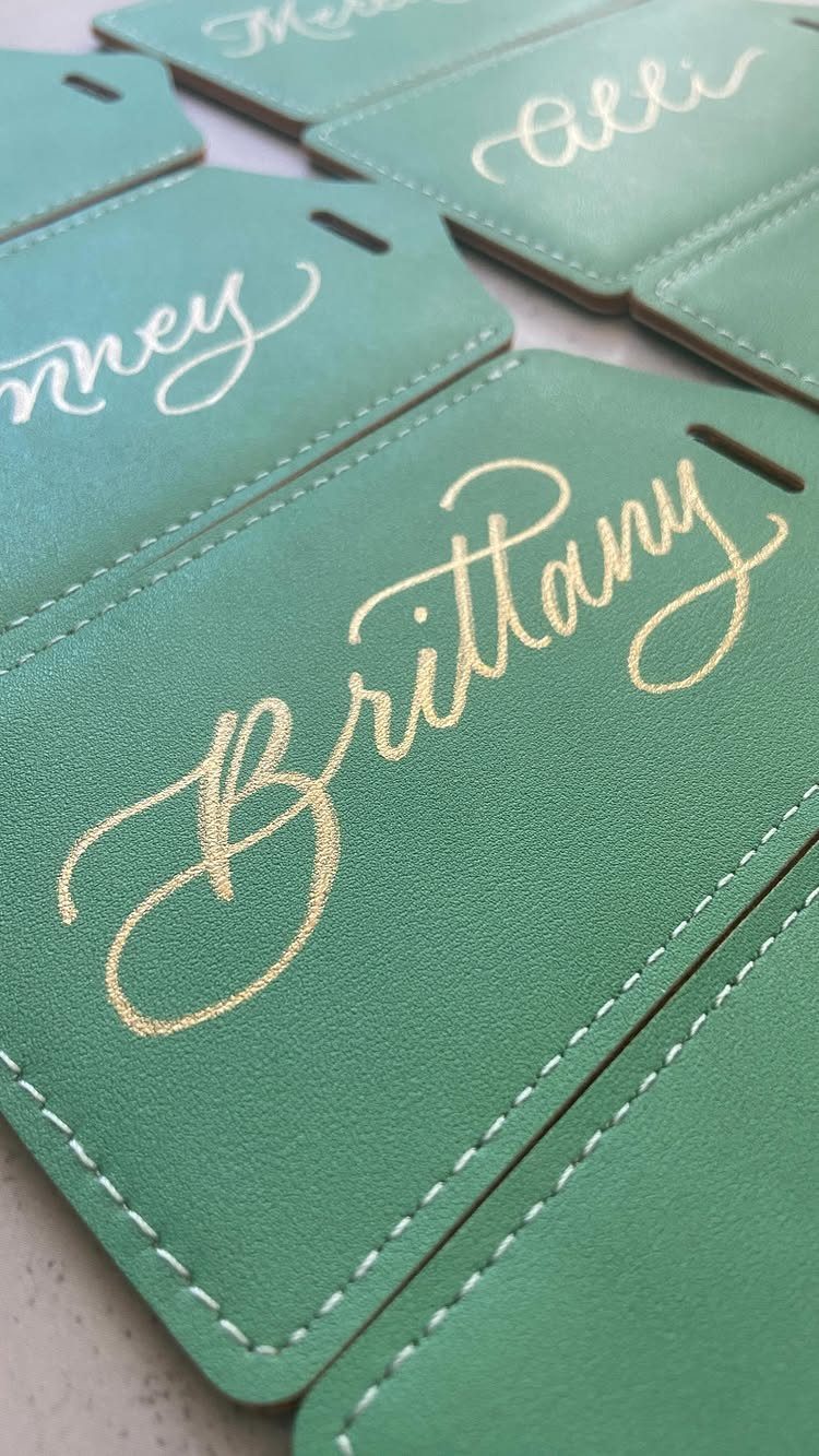 Green faux-leather luggage tags with personalized names written in gold and white calligraphy.