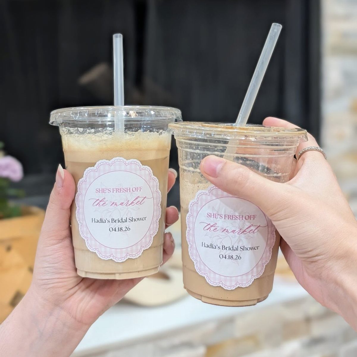Two iced coffee drinks in plastic cups with bridal shower labels and straws.
