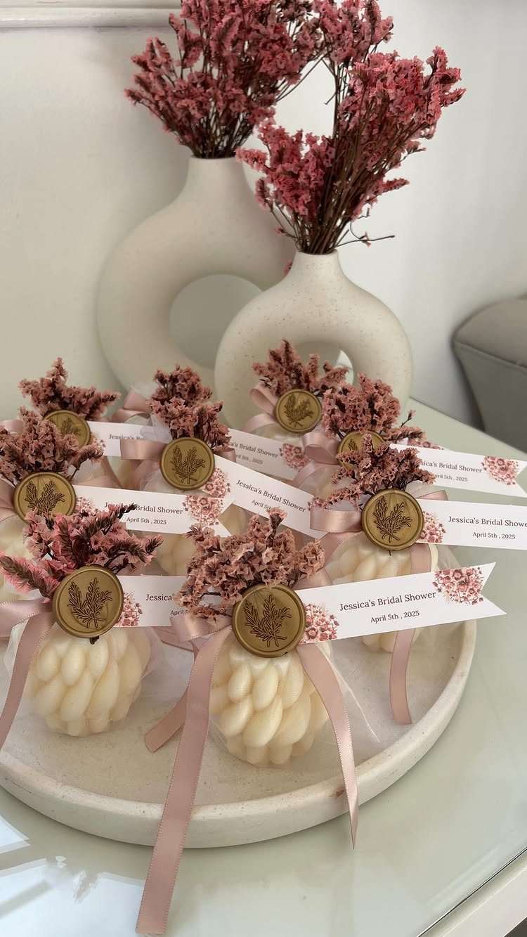 Small white textured candles with pink ribbons and dried flowers on a platter.
