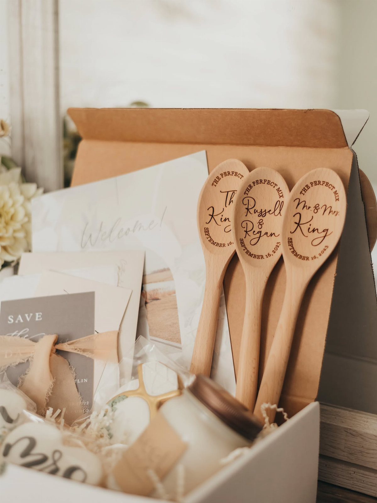 Three engraved wooden spoons standing in a white gift box with a candle.
