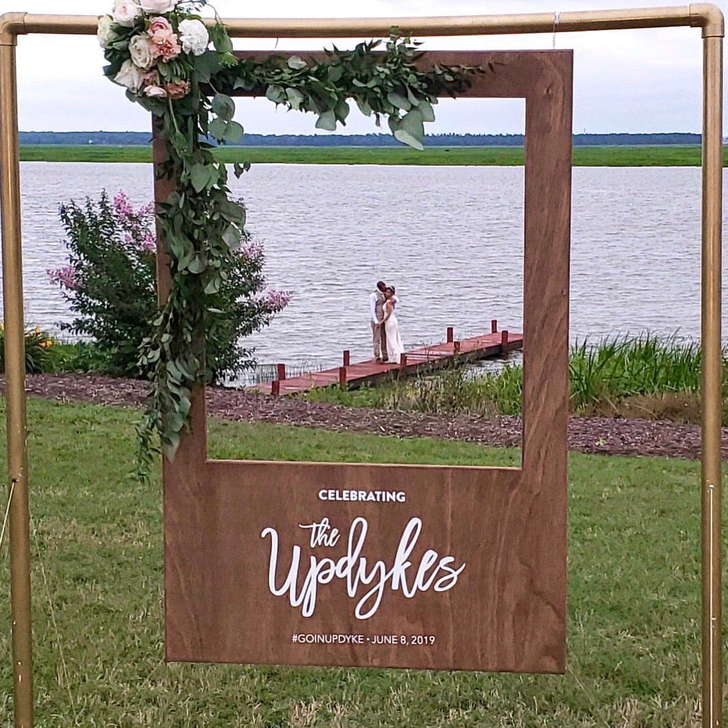 Wooden photo frame backdrop with floral decorations framing a couple by a lake