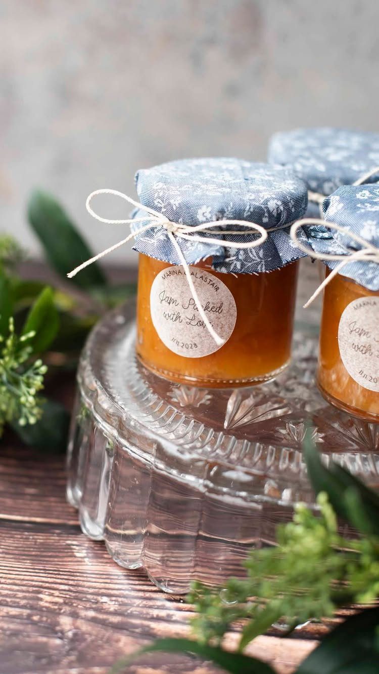 Small jars of orange jam with fabric lids and twine on glass stand.