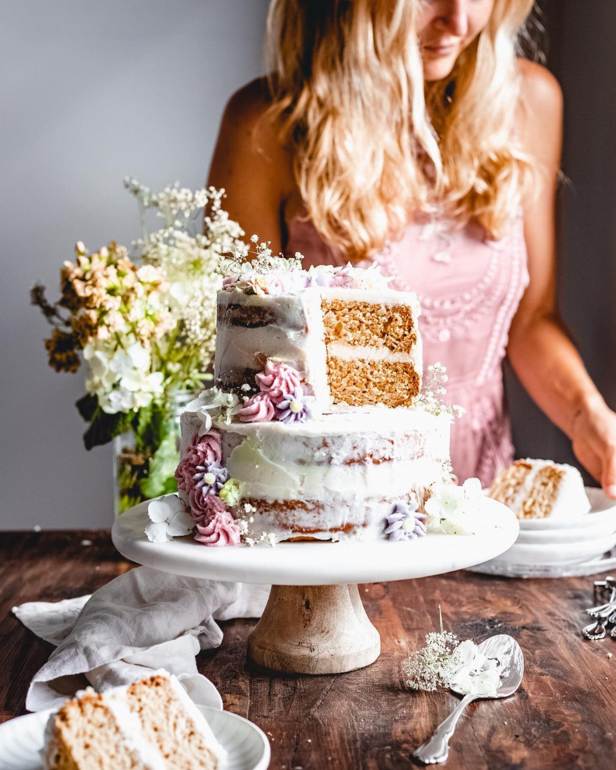 Two-tier semi-naked wedding cake with purple flowers on a rustic wooden table.
