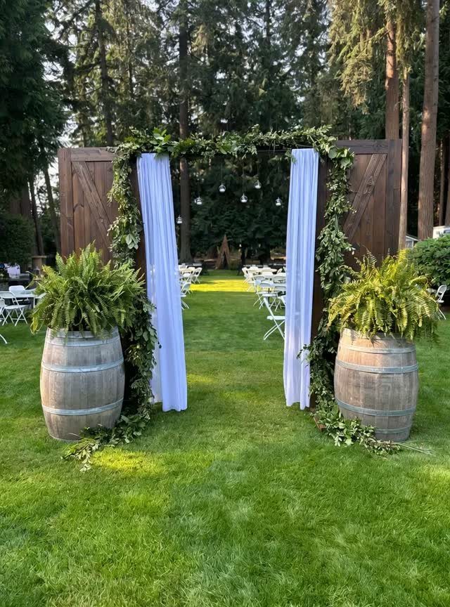 Wooden wedding arch with white curtains and greenery on a grassy lawn