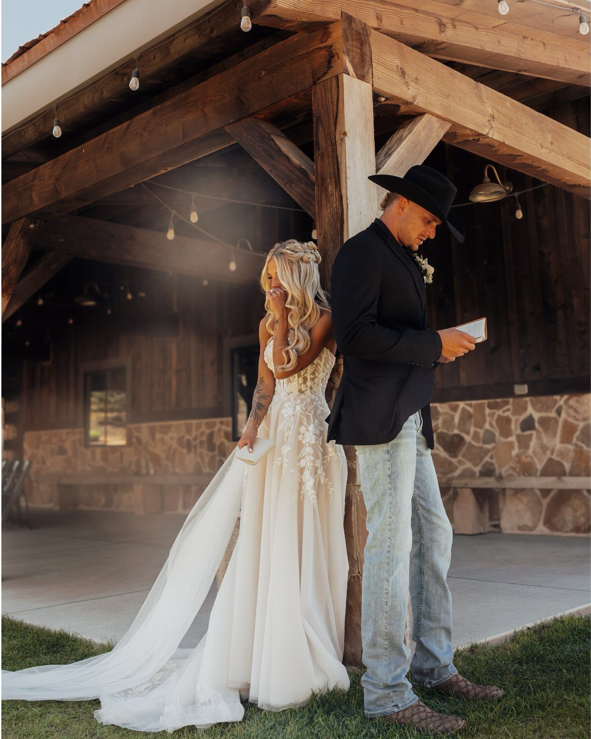 Bride in lace gown and groom in cowboy hat and jeans standing back-to-back.