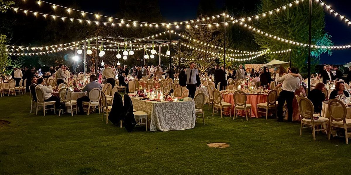 Outdoor wedding reception at night with warm string lights draped over dining tables.