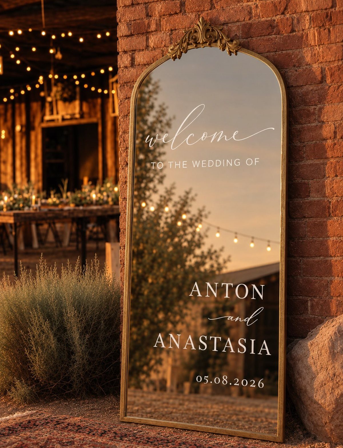 Gold-framed vintage mirror welcome sign leaning against a brick wall at a wedding