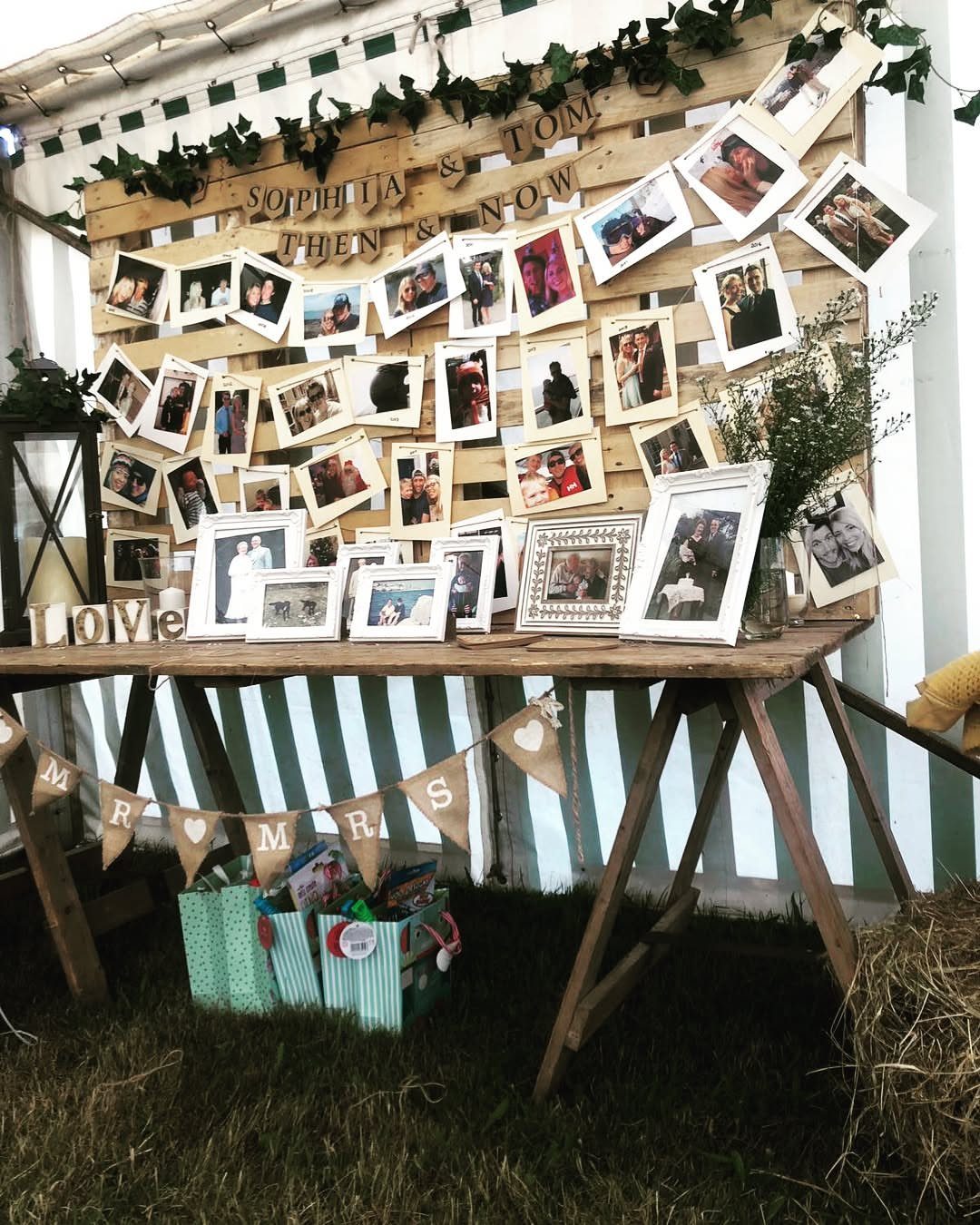 Wooden pallet wall displaying couple's photos behind a rustic table with framed pictures.