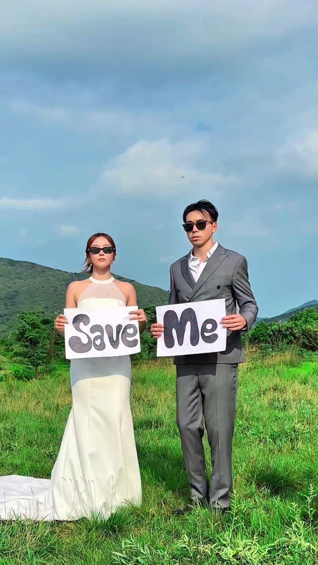 Couple in wedding attire holding signs that say Save Me in a field