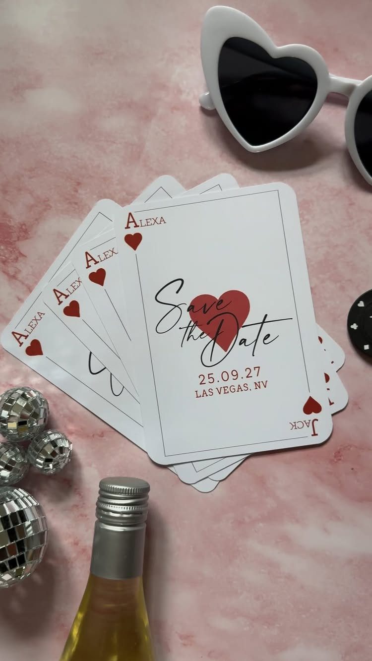 Playing card save the date cards with red hearts on pink marble surface.