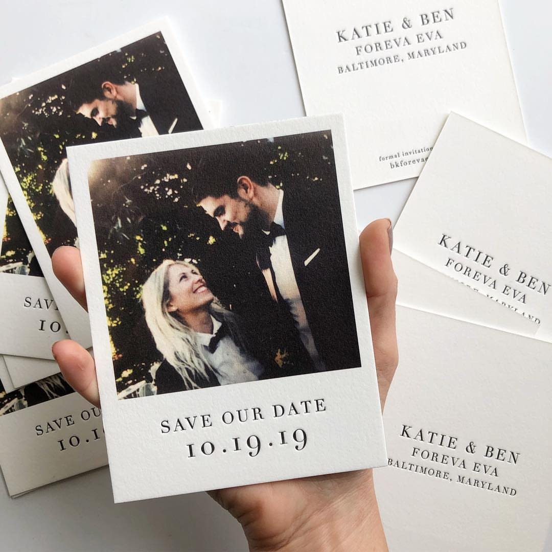 Polaroid-style save the date card held by a hand among other wedding stationery.