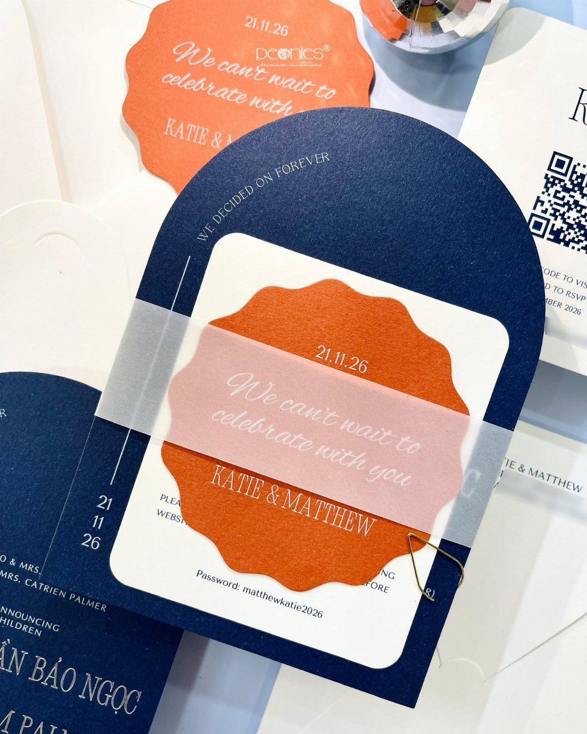 Arched navy blue wedding invitation with a scalloped orange insert and vellum band.