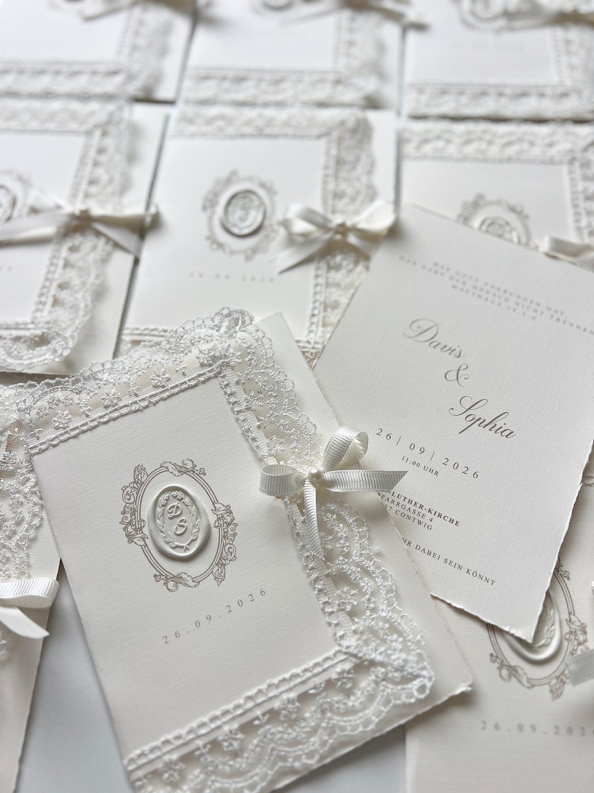 White wedding invitations with lace borders, satin ribbons, and elegant wax seals.