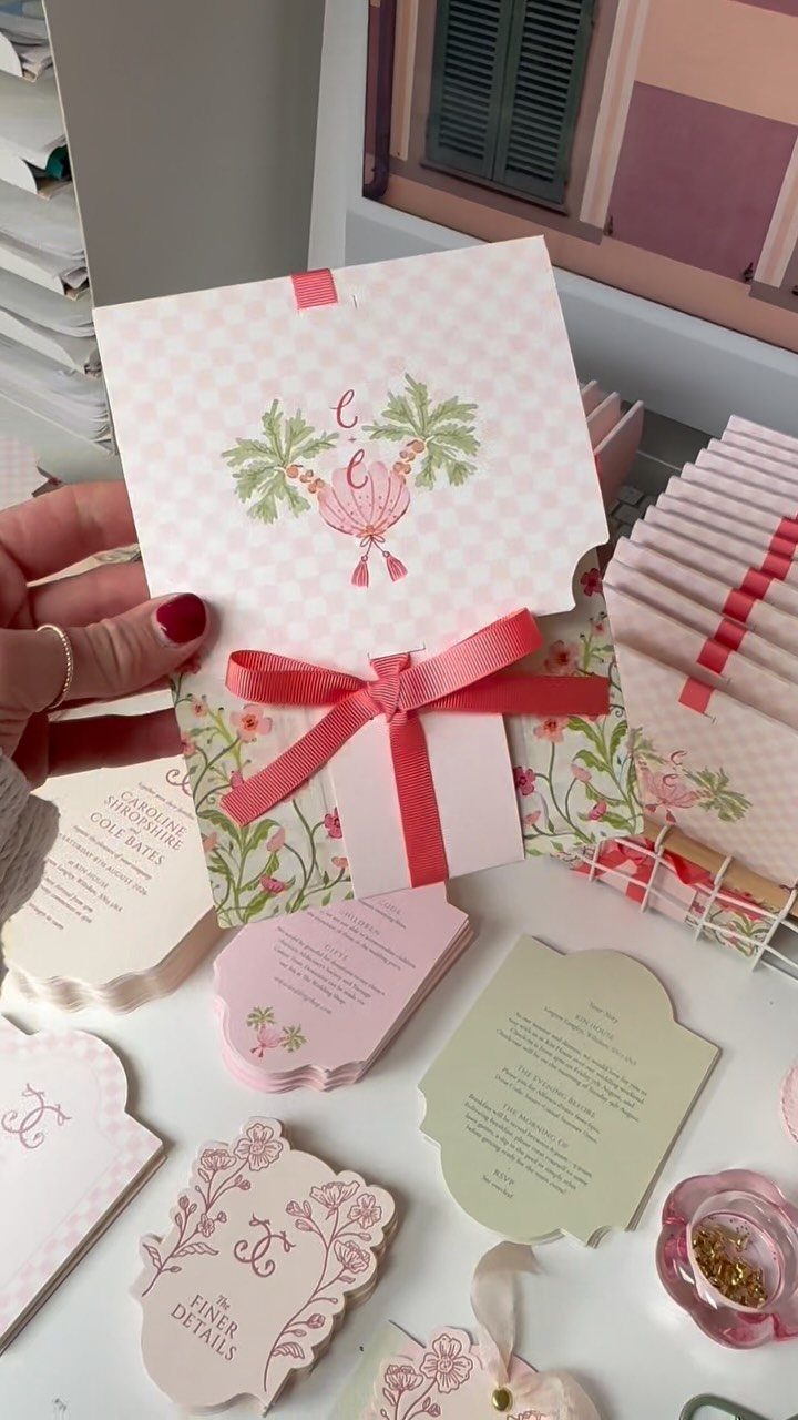 Wedding stationery suite with pink checkered invitations and floral die-cut cards tied with ribbon.