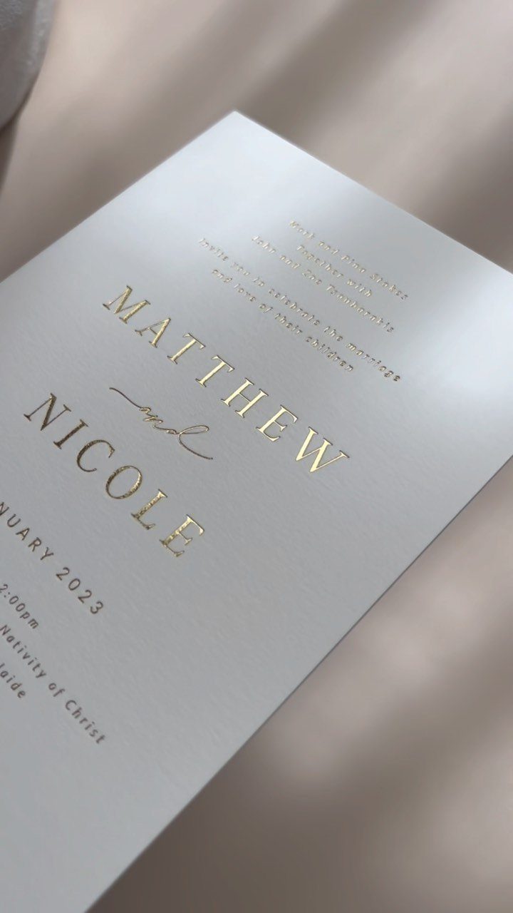 White wedding invitation with gold foil names resting on beige satin fabric