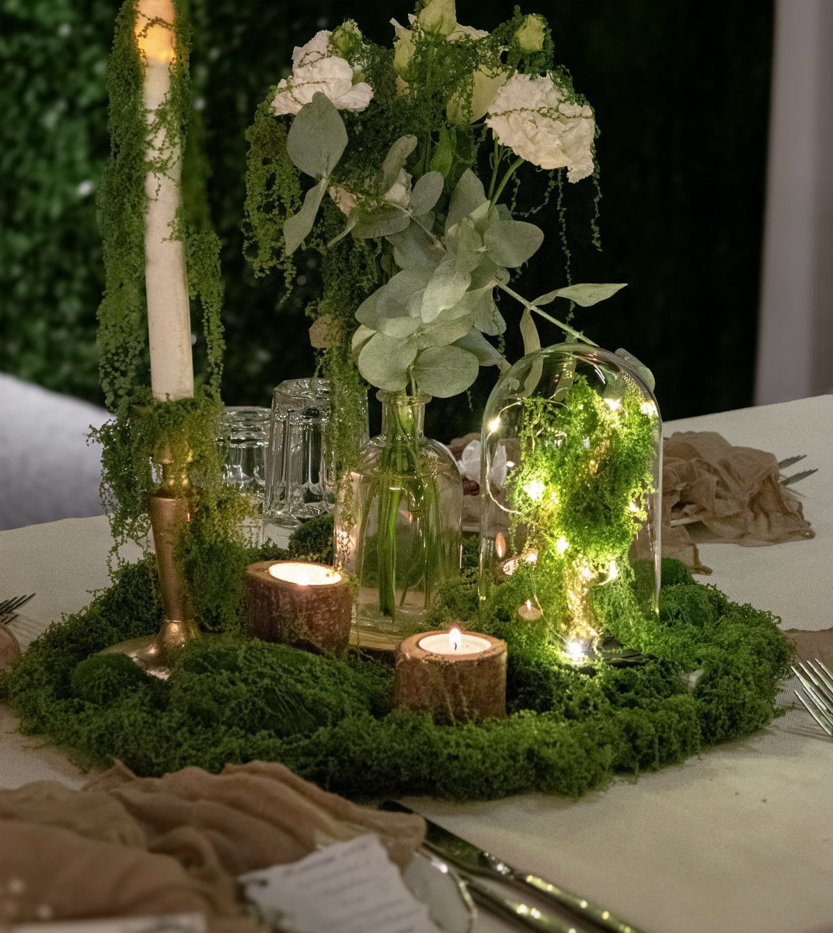 Mossy wedding centerpiece with white flowers, tea lights, and a glass cloche enclosure.