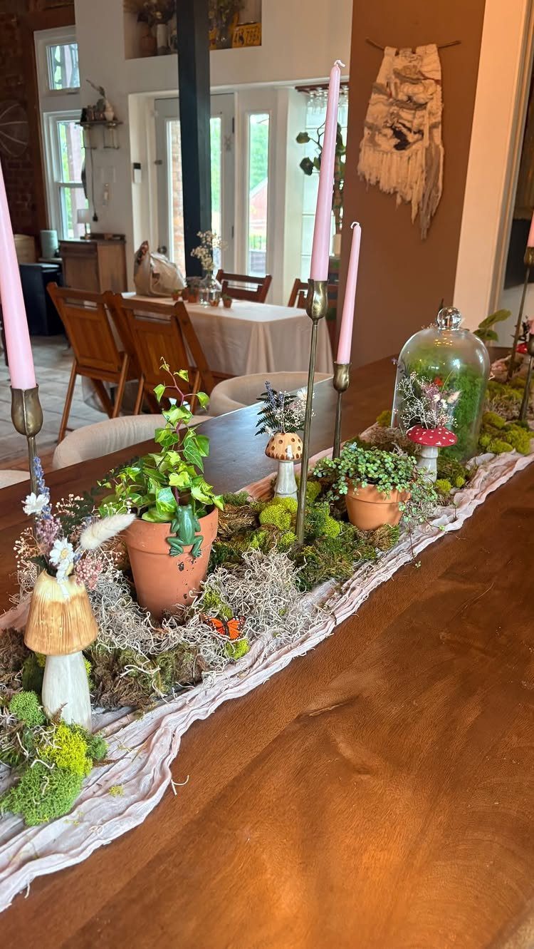 Mossy table runner with small potted plants, mushrooms, and pink candles for wedding decor