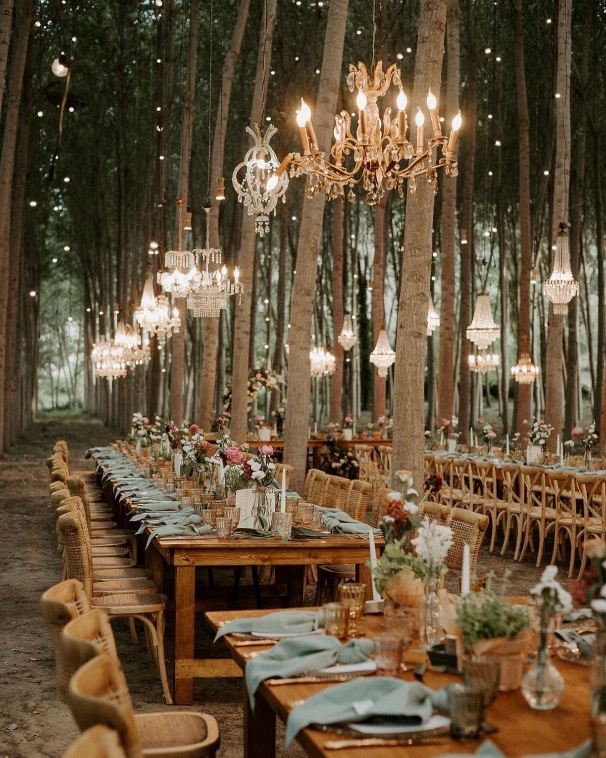 Wooden wedding tables with greenery and chandeliers set among tall forest trees