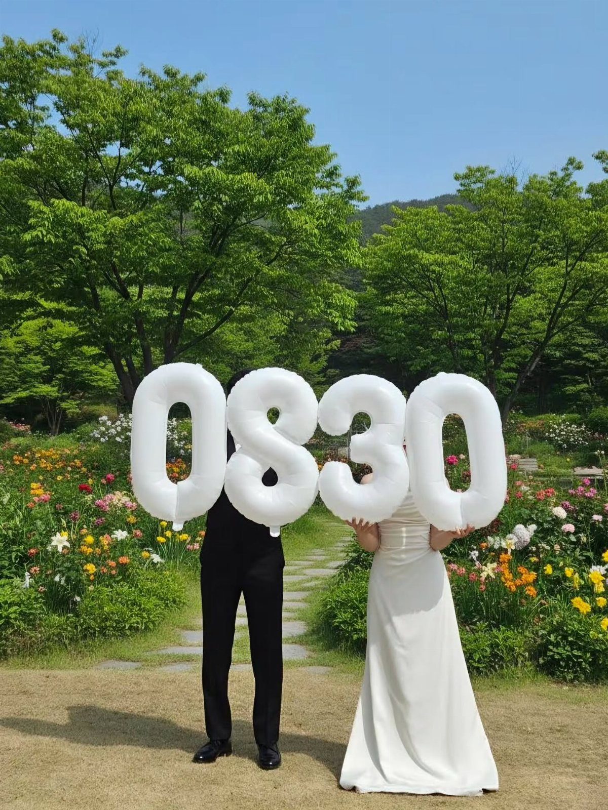 Couple in a garden holding large white balloons spelling out the date 0830.