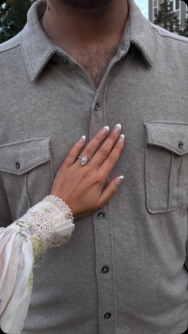Hand with diamond engagement ring resting on a person's grey button-down shirt