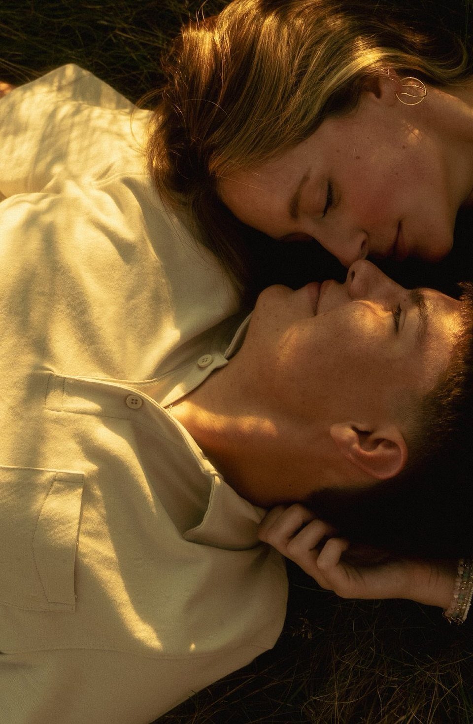 Couple lying on grass with foreheads touching in warm golden sunlight.