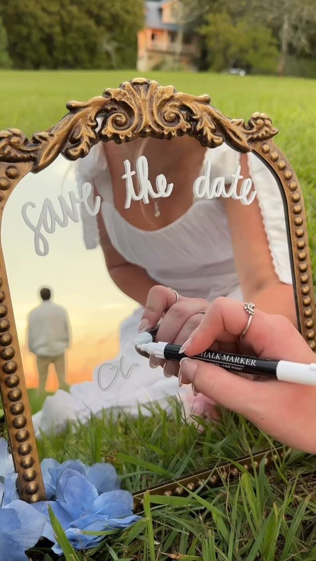 Hand writing save the date on a gold mirror reflecting an engaged couple.