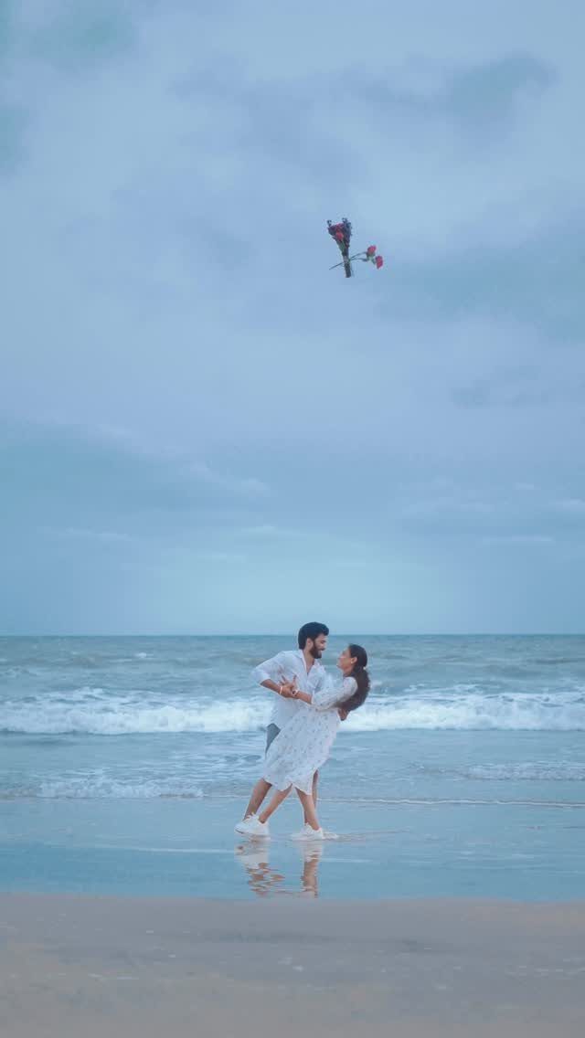 Couple in white embracing on a beach with flowers floating in the air