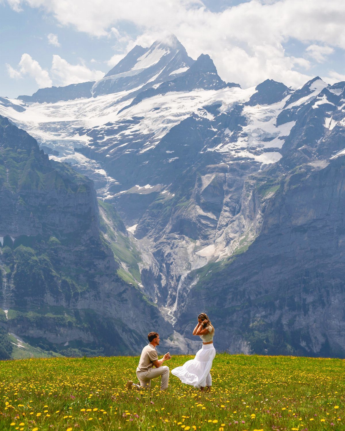Man proposing to woman in a wildflower meadow with epic snow-capped mountains behind.