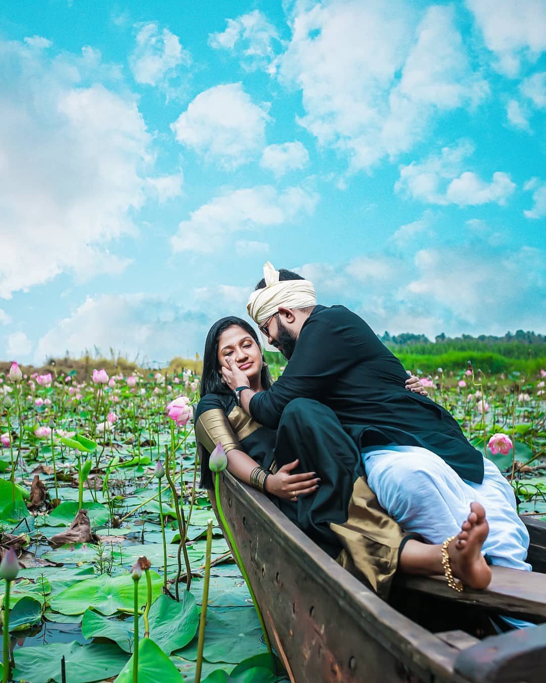 Couple in traditional attire posing in a boat among pink lotus flowers.
