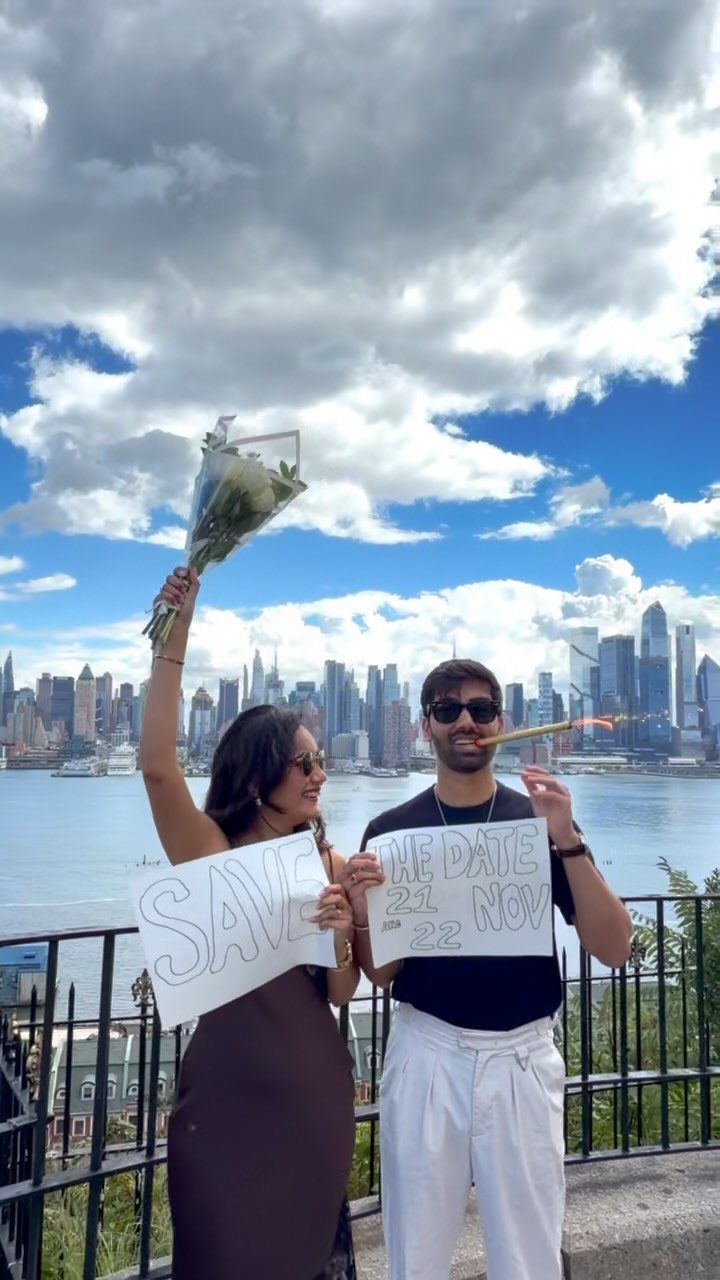 Couple holding a save the date sign with a city skyline in background
