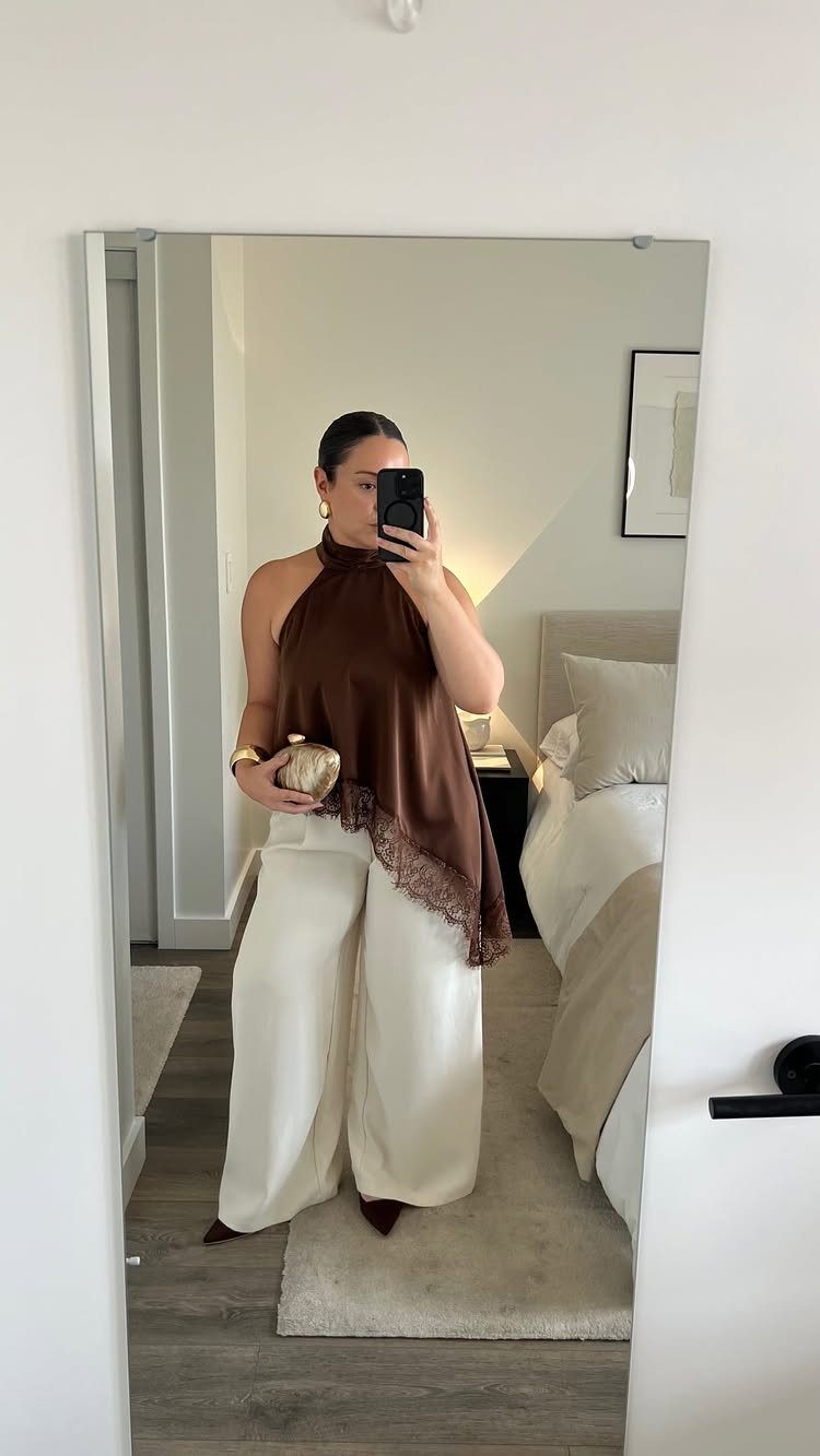 Woman in brown satin halter top and cream wide-leg trousers taking mirror selfie.
