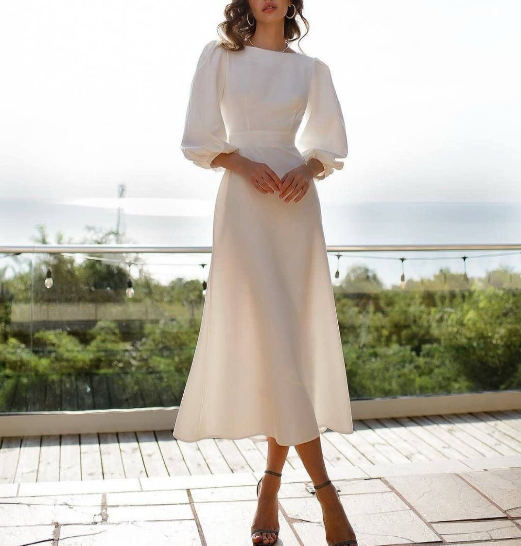 Woman in a white long-sleeve midi dress standing on a sunny outdoor deck.