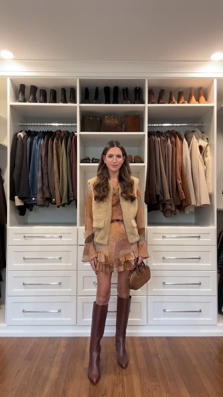 Woman wearing a brown patterned dress, tan fur vest, and tall brown boots.