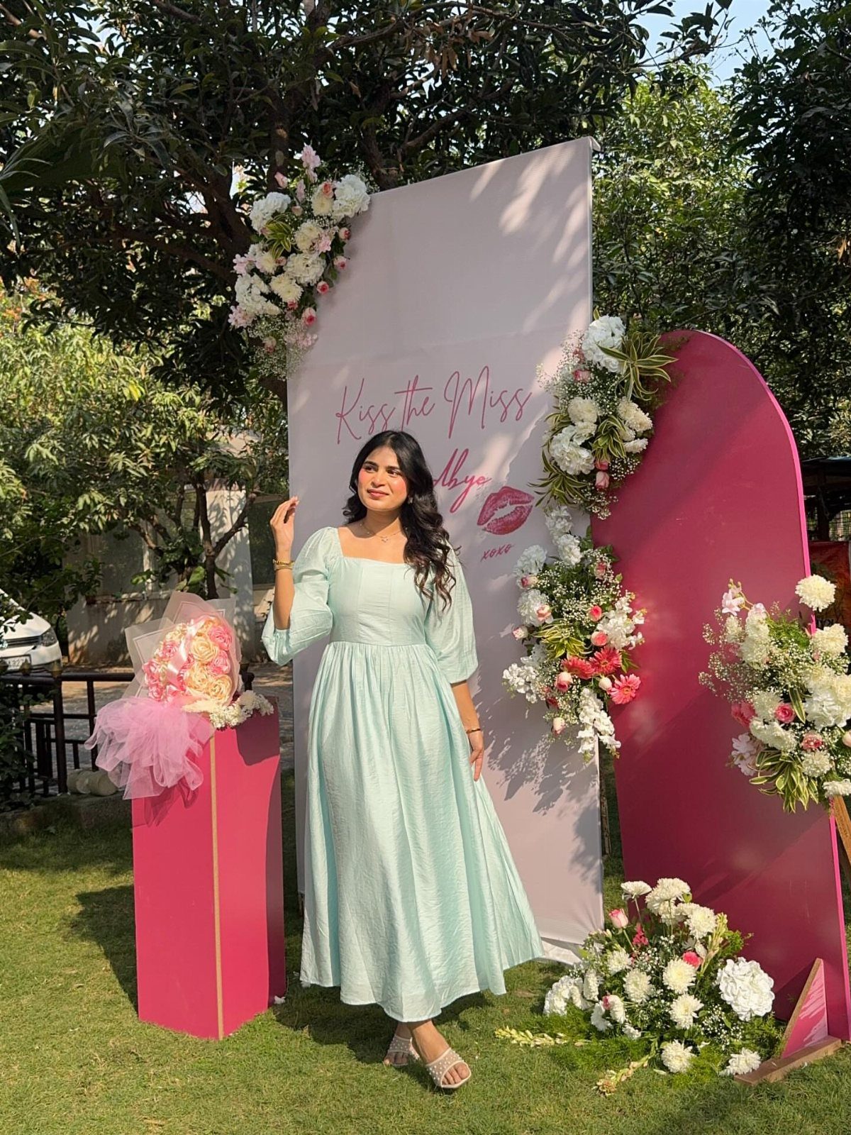 Woman in light blue midi dress posing before a floral bridal shower backdrop.
