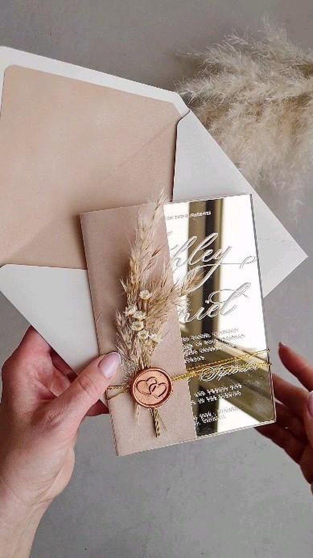 Gold acrylic wedding invitation with wax seal and dried grass held by hands