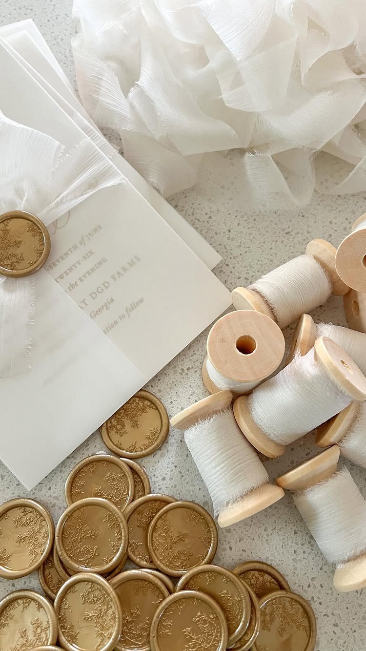 White wedding invitation wrapped in translucent vellum paper with gold wax seals.