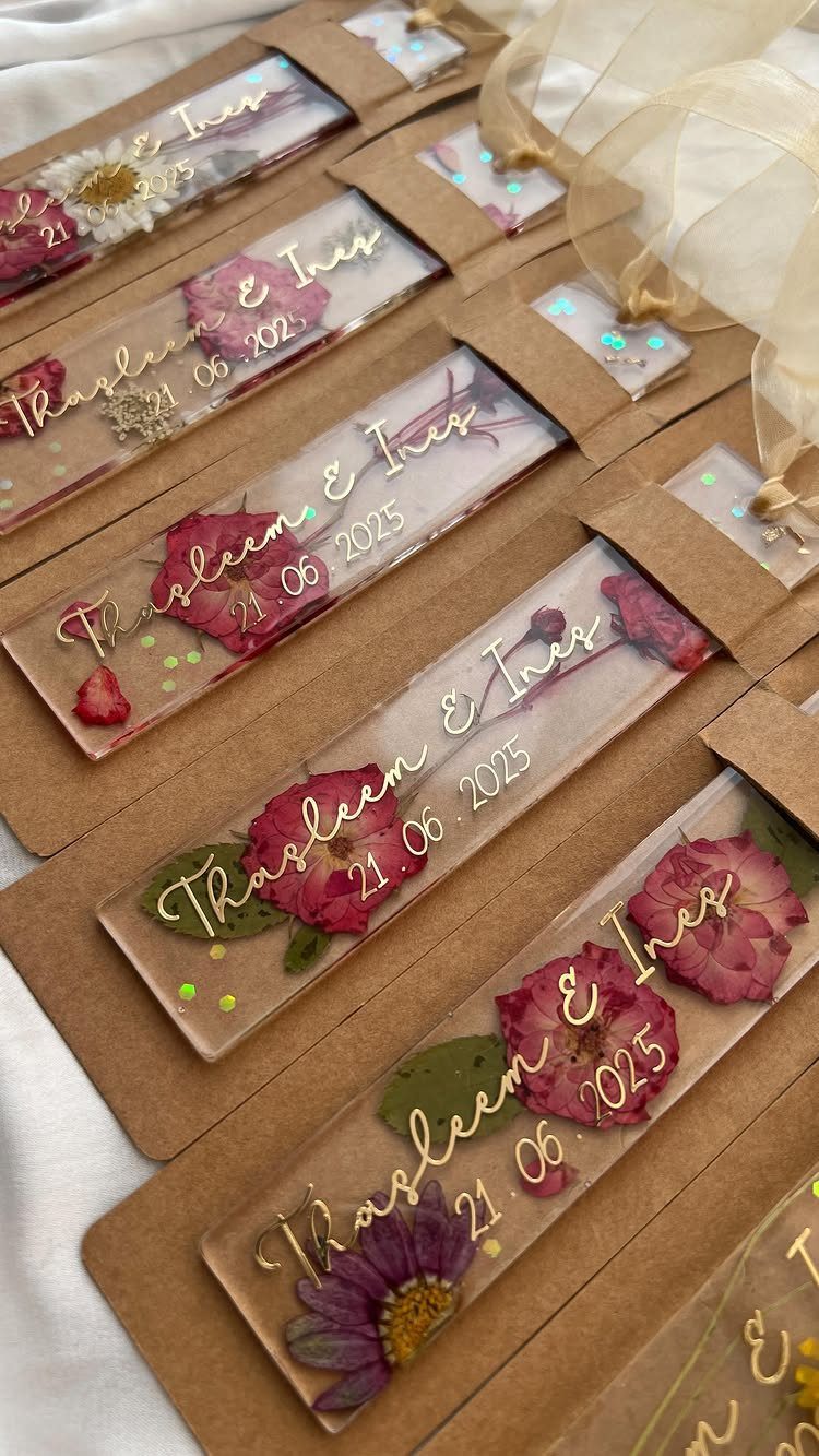 Clear resin bookmarks with dried flowers and gold lettering in brown cardboard sleeves.
